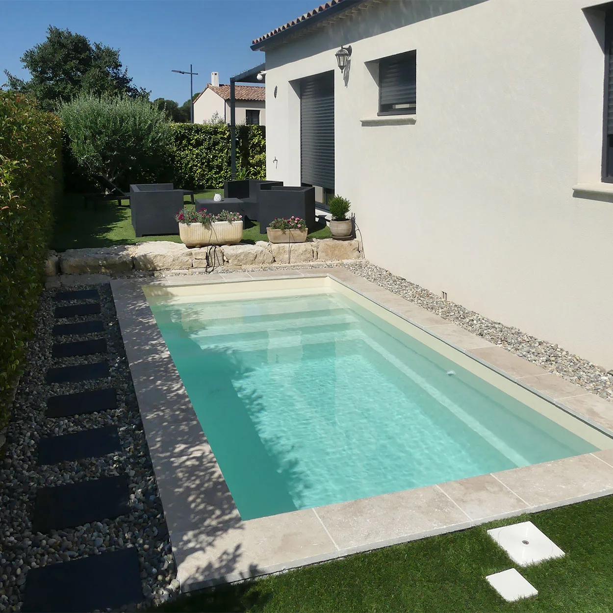 Installation d'une petite piscine Extra 45 entre une haie et une façade de maison.