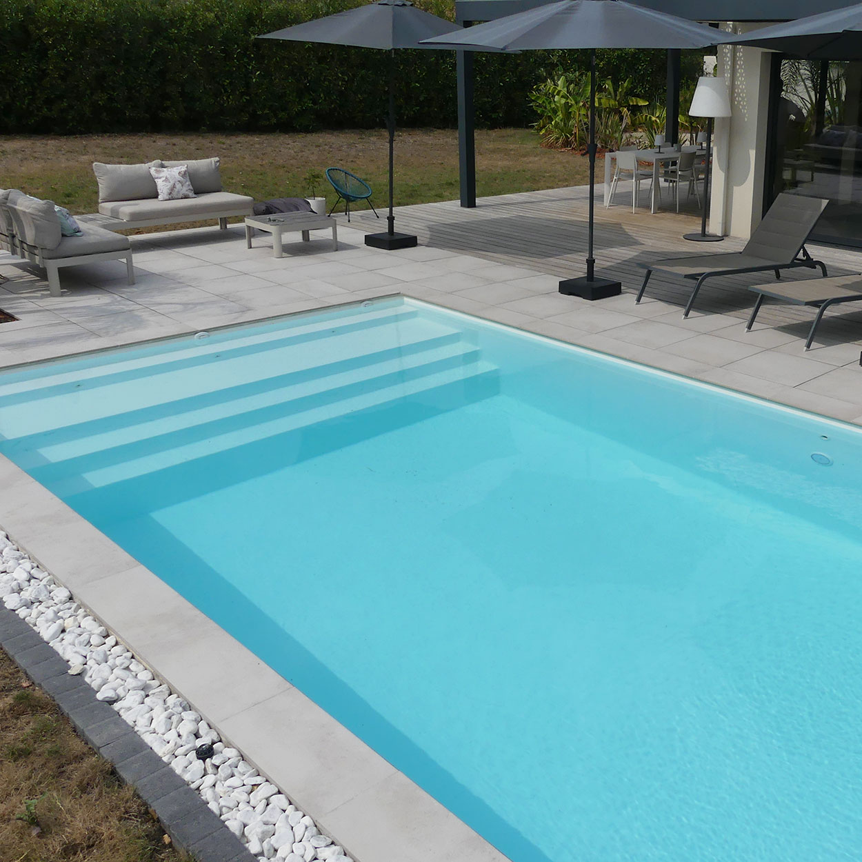 Aménagement moderne d'une piscine Figuerolle avec plage, transats et parasols.