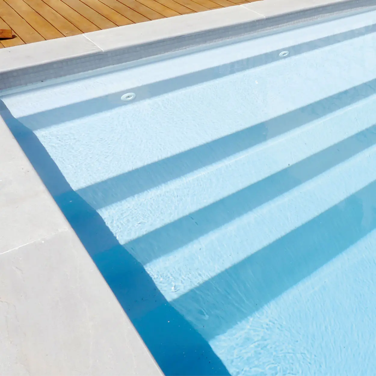 Zoom sur l'escalier latéral et la banquette immergée de la piscine coque Inizan.