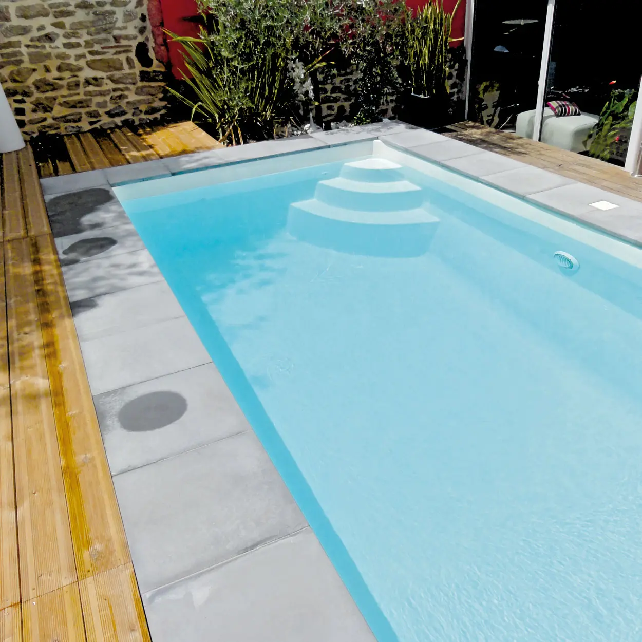 Piscine Méjean avec margelles en grès cérame et terrasse en bois naturel.