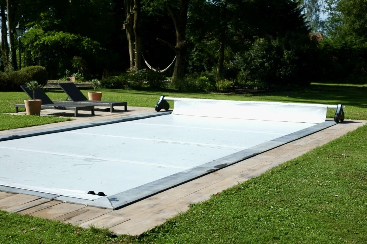 Enrouleur motorisé Koverloop Assist installé sur une piscine rectangulaire avec couverture gonflable grise et plage en bois.