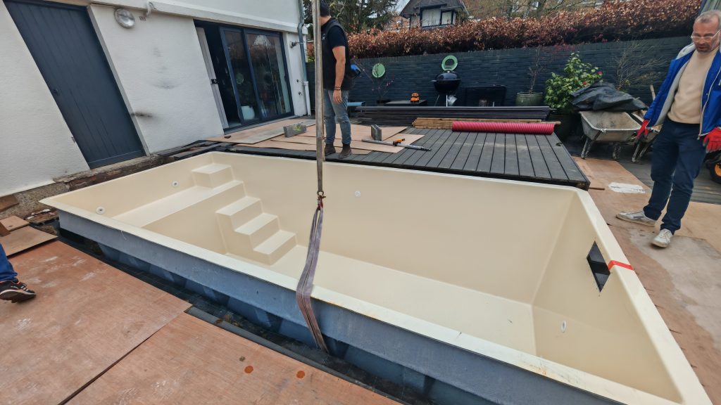 Pose d'une mini piscine coque sur son radier de niveau au milieu d'une terrasse en cours de rénovation.