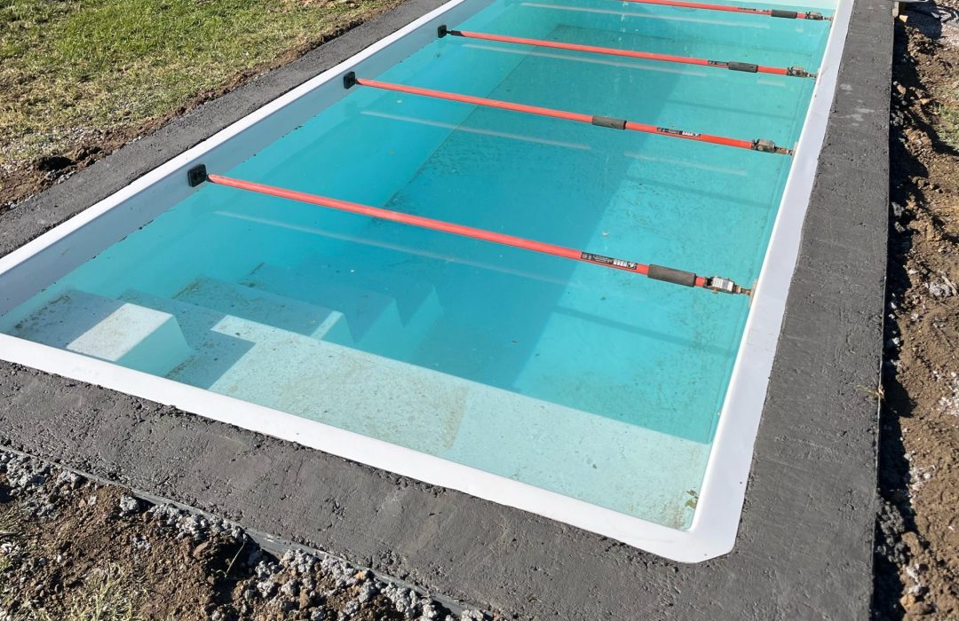 Bassin de piscine coque à Caudry en pleine mise en eau, maintenu par quatre étais de sécurité horizontaux rouges pour préserver sa forme.