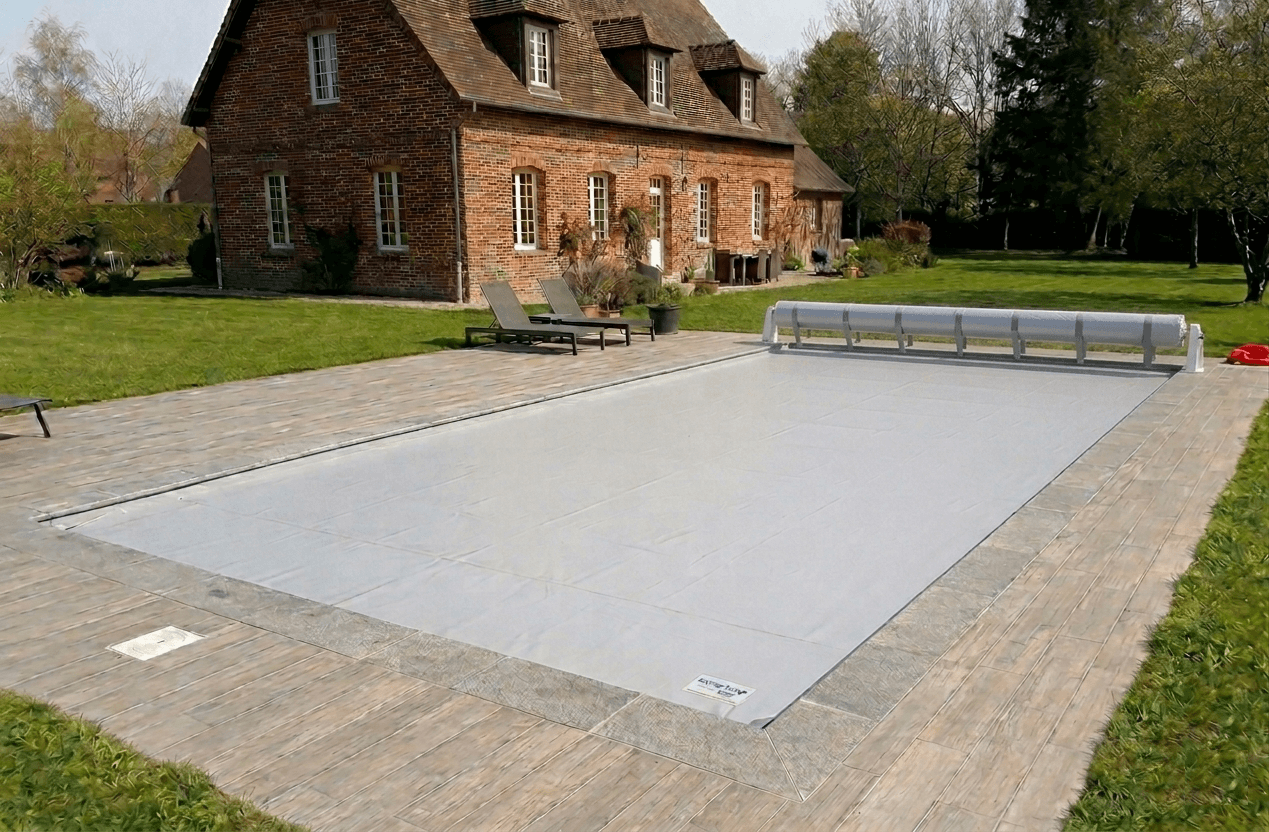 Couverture de sécurité piscine gonflable Koverloop grise installée sur une piscine rectangulaire devant une maison en briques dans le Nord.