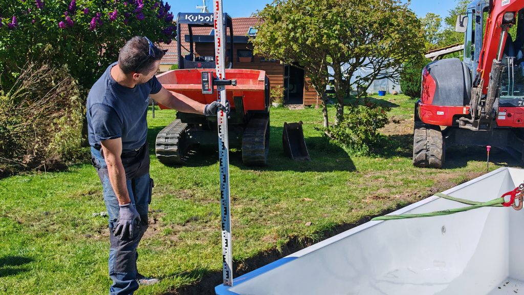Technicien utilisant une mire et un laser pour vérifier le niveau de la piscine Mini Couloir à Caudry.